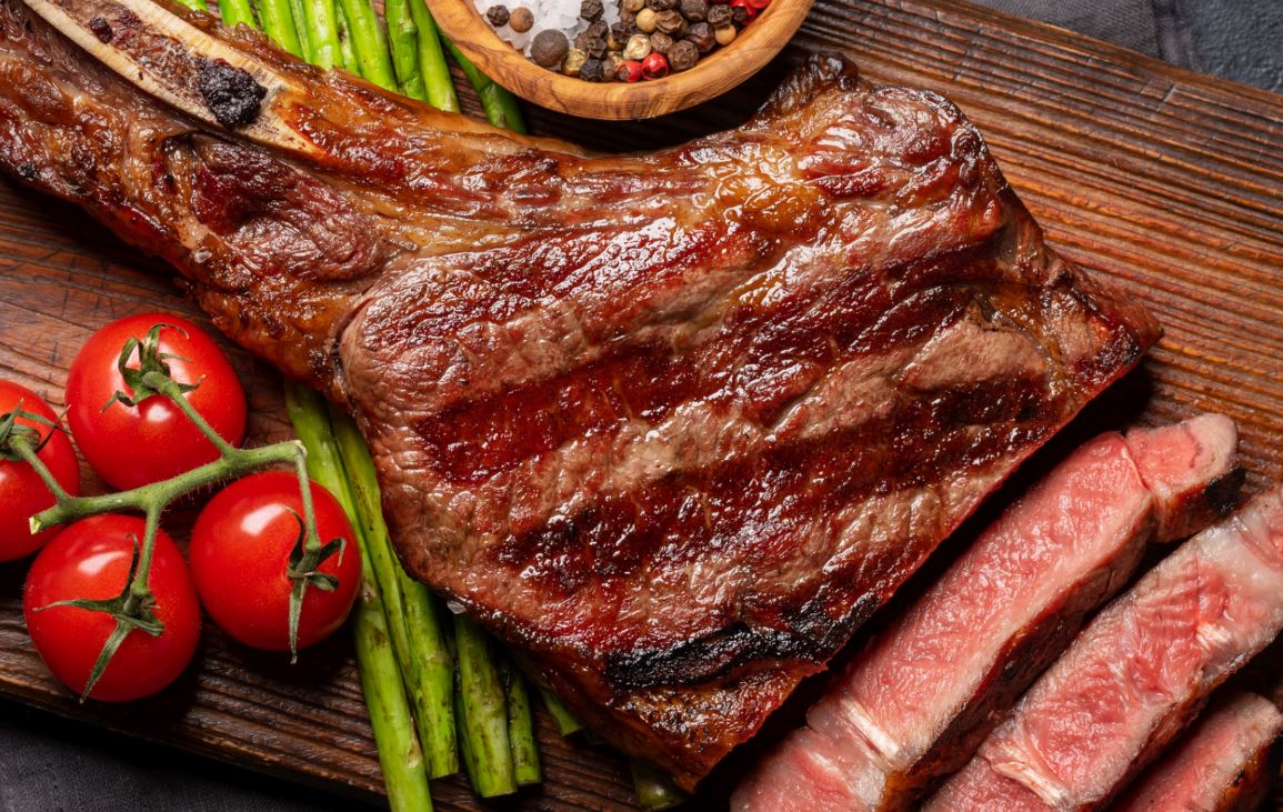 Succulent steak on a chopping board with tomatoes, asparagus & peppercorns